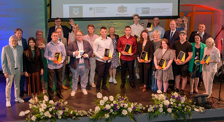Preisträgerinnen, Preisträger, Jury und Laudatoren des Berufsbildungspreis Lettland 2024 stehen nebeneinander auf einer Bühne und lächeln in die Kamera. Die Gewinner und Gewinnerinnen halten ihre Preise in den Händen.