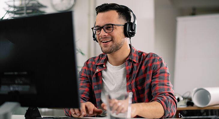 ein Foto mit einem jungen Mann, der vor einem Monitor sitzt und ein Headset trägt