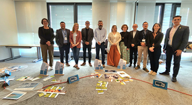 Group of people (the Costa Rican delegation with GOVET colleagues) standing smiling behind the VET Chain Tool scenario - ropes with supply chain stations in the workshop room