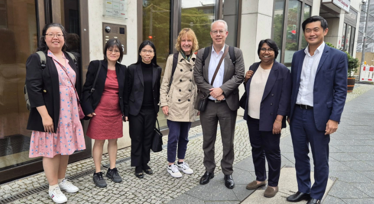 Group of 7 smiling people (Singapourian delegation with GOVET colleagues) standing in front of an office building